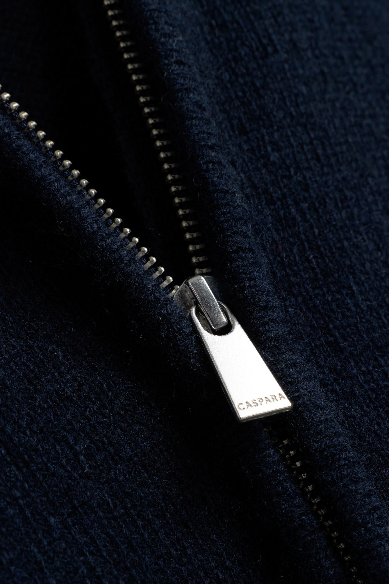 Close-up of the silver zipper pull engraved with CASPARA logo on a navy woolknit jacket.
